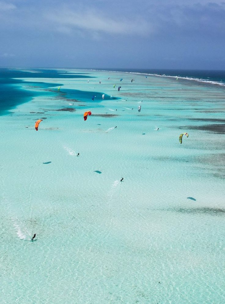 Vista aérea de un banco de arena larguísimo en agua turquesa, con cometas de kitesurf