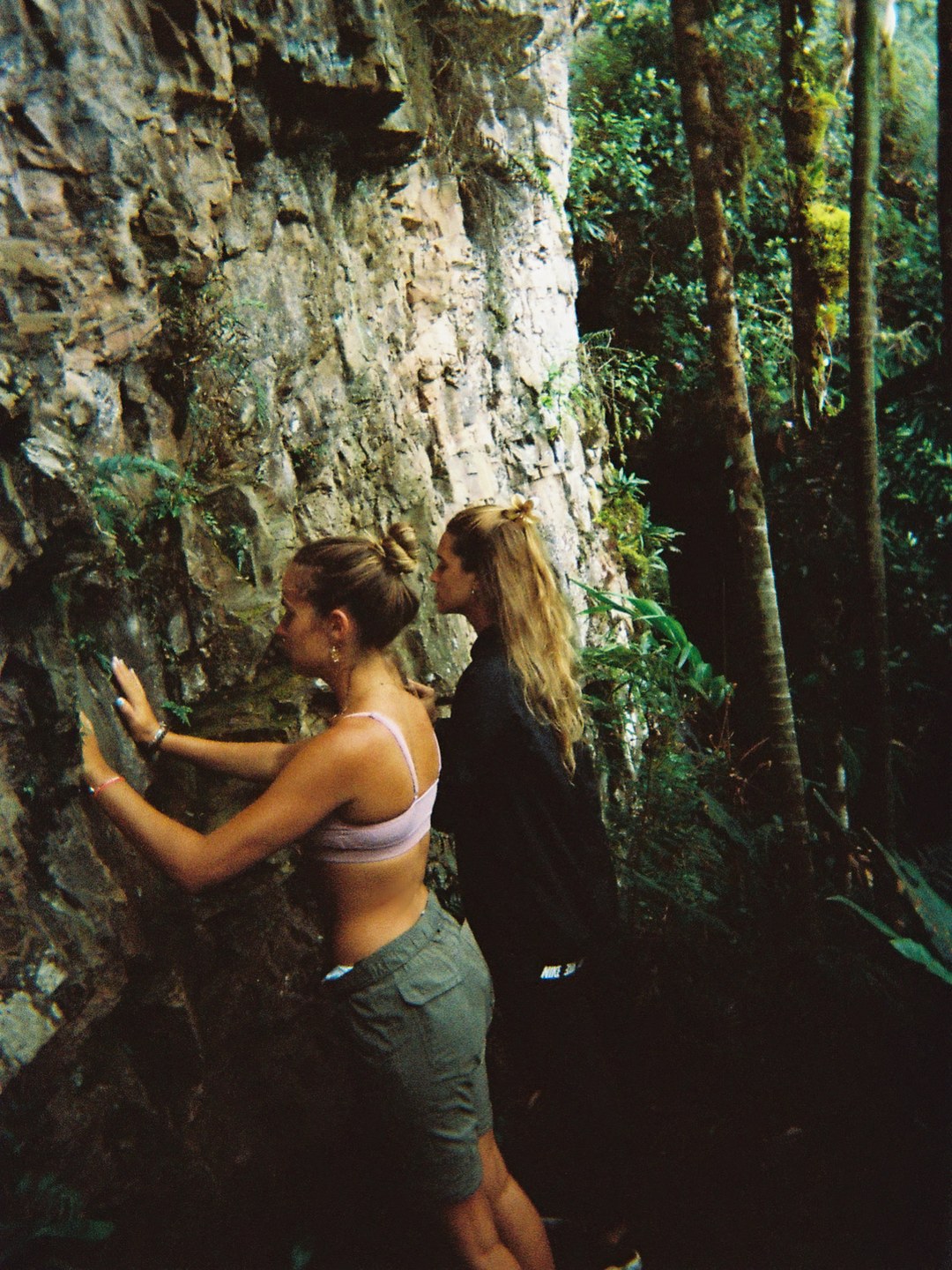 Dos viajeras con la mano en la pared de roca del tepuy, entre la selva